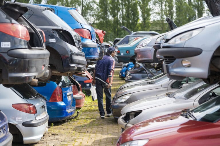 Person inspecting stacked cars in a salvage yard.