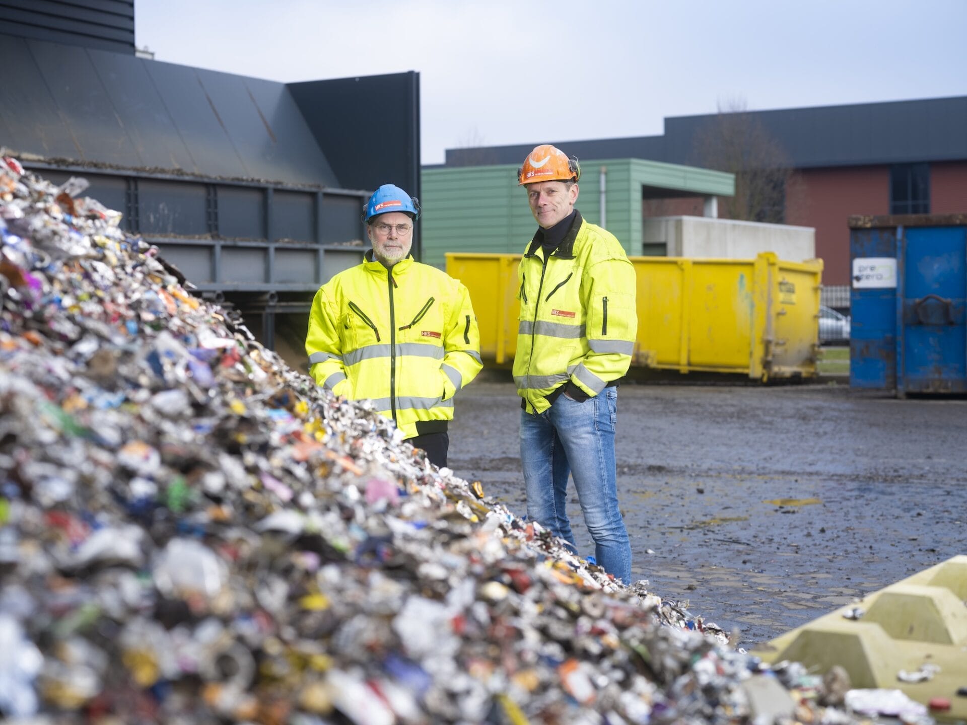 Twee mannen bij recyclingcentrum met afvalhopen